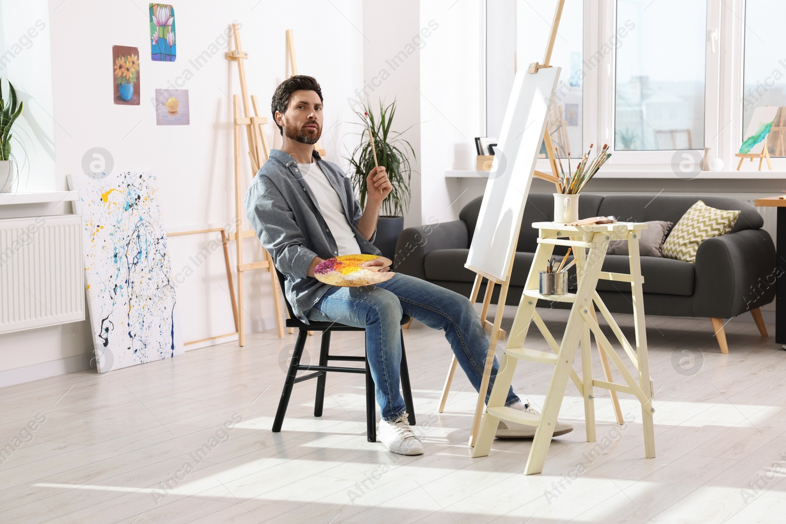 Photo of Man painting in studio. Using easel to hold canvas