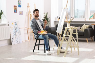 Photo of Man painting in studio. Using easel to hold canvas