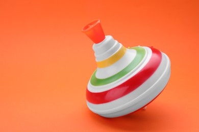 Photo of One bright spinning top on orange background, space for text. Toy whirligig
