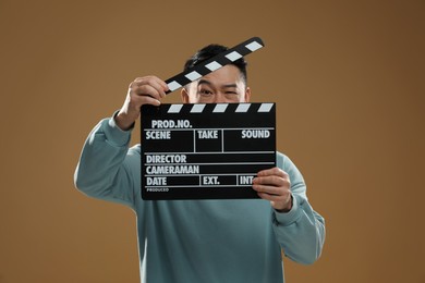 Photo of Emotional asian actor with clapperboard on brown background. Film industry