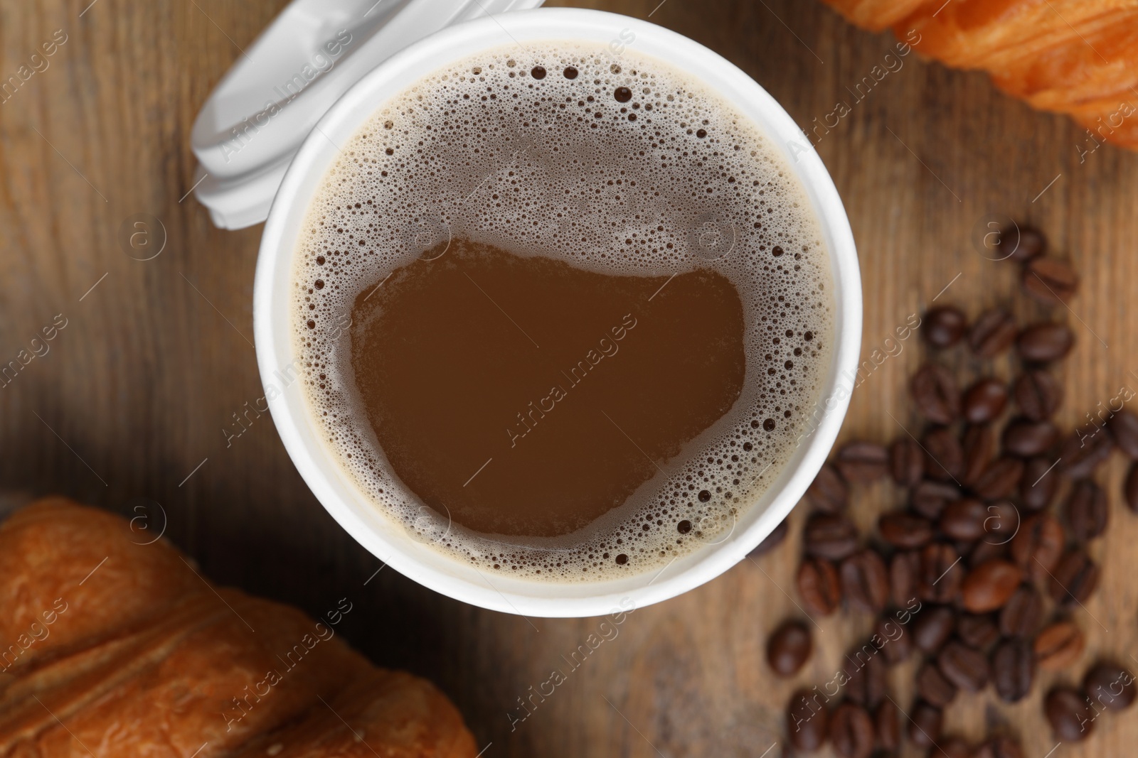 Photo of Coffee to go. Paper cup with tasty drink, pastry and beans on wooden table, flat lay