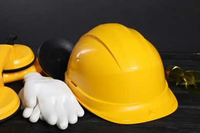 Photo of Hard hat, suction lifters, protective gloves and goggles on black wooden surface against gray background, closeup