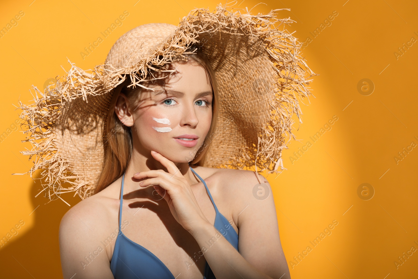 Photo of Beautiful young woman in straw hat with sun protection cream on her face against orange background