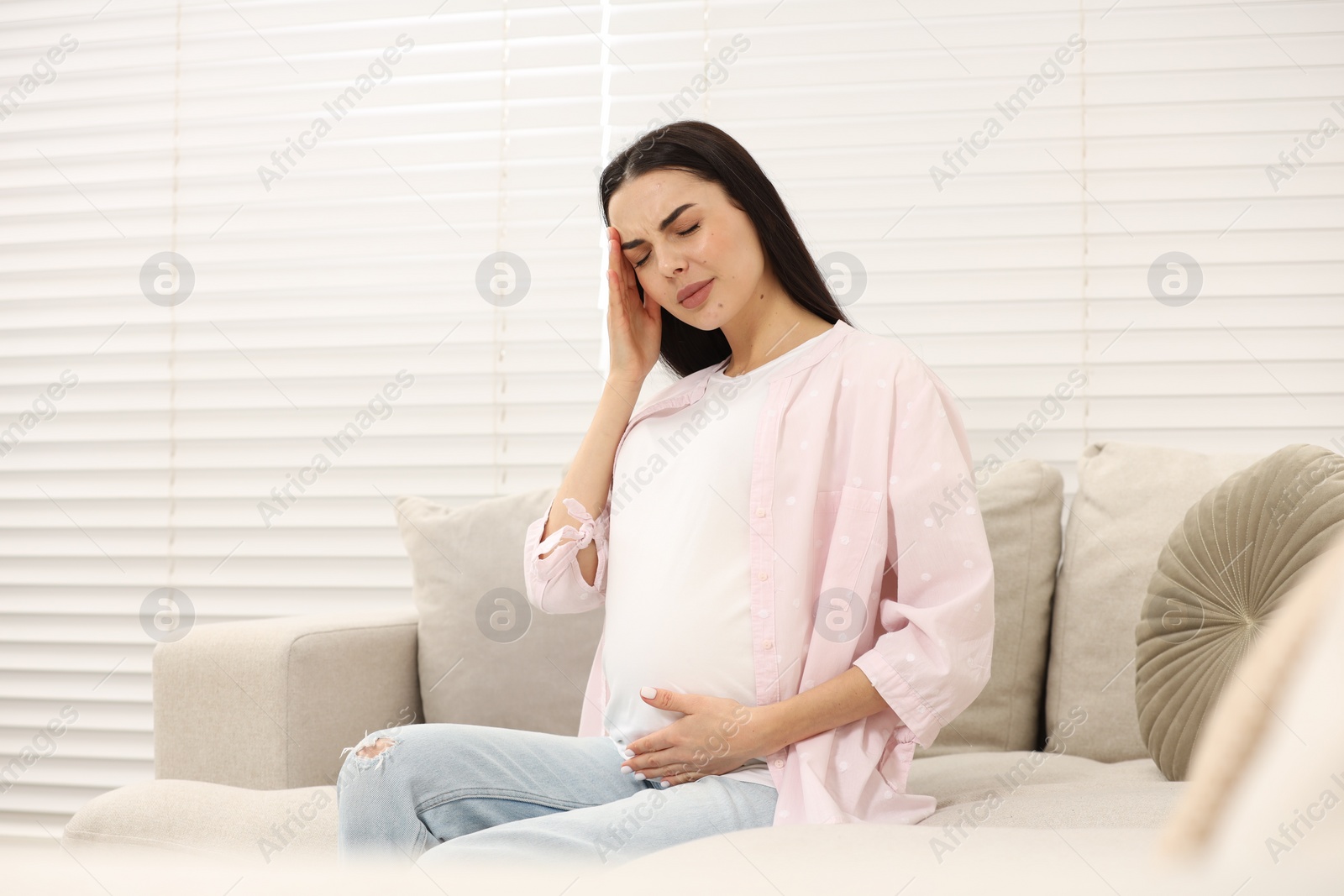 Photo of Pregnant woman suffering from headache on sofa at home