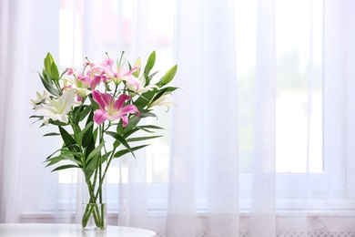 Vase with bouquet of beautiful lilies on white table indoors. Space for text