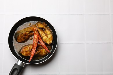 Photo of Tasty fish curry in frying pan on white tiled table, top view. Space for text. Indian cuisine