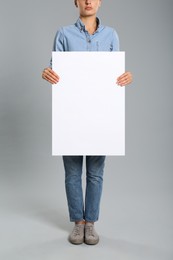 Woman holding white blank poster on grey background, closeup. Mockup for design