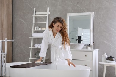 Photo of Beautiful woman in soft white robe near bathtub at home