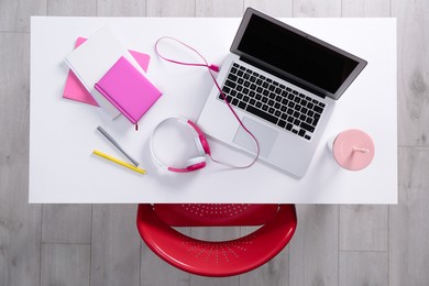 Chair near white table with laptop, headphones and stationery indoors, top view