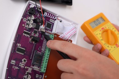 Man using digital multimeter while installing home security alarm system on white wall indoors, closeup