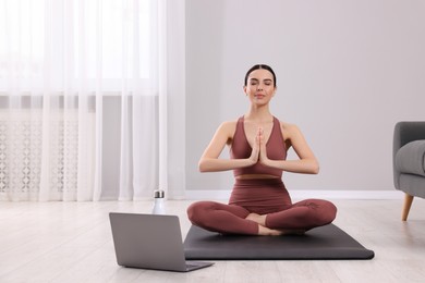 Woman in sportswear meditating near laptop at home, space for text