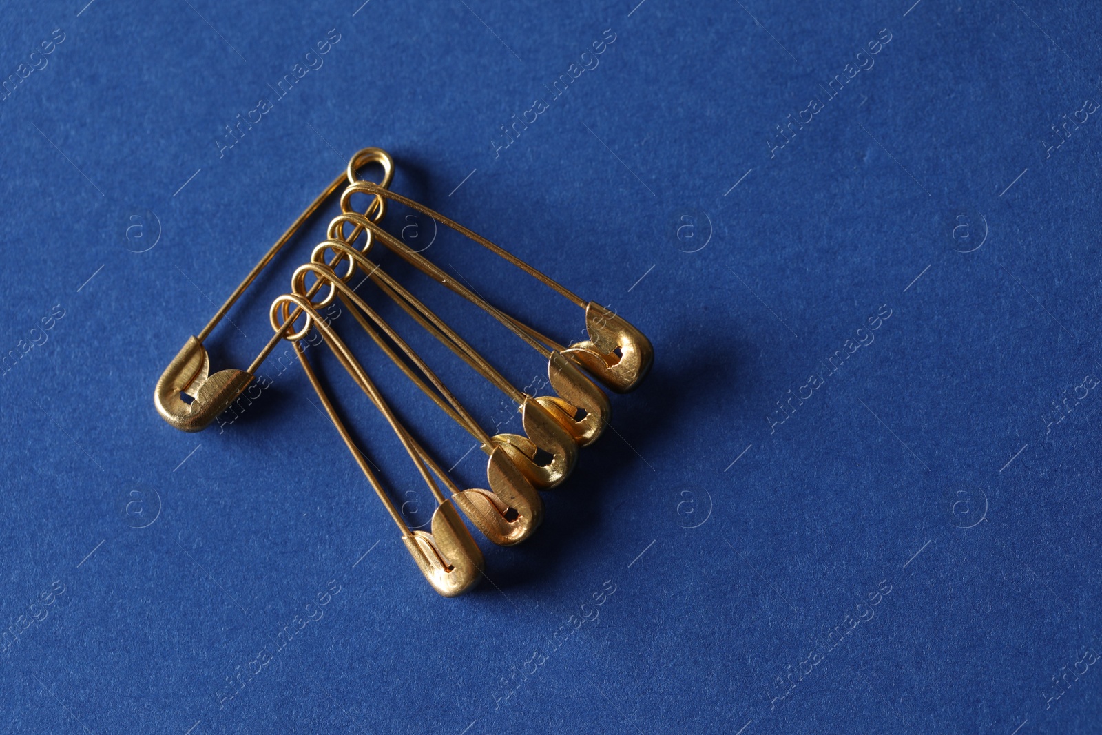 Photo of Golden safety pins on blue background, flat lay. Space for text