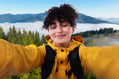 Beautiful young woman taking selfie in mountains