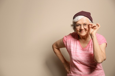 Portrait of elderly woman in hipster outfit on color background. Space for text