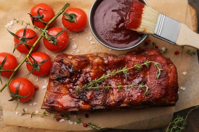 Photo of Tasty roasted pork ribs served with sauce and tomatoes on table, top view