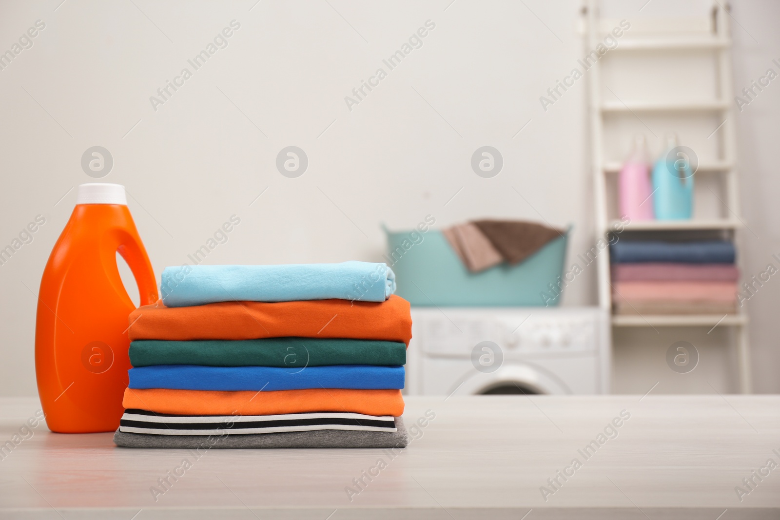 Photo of Stack of fresh laundry and detergent on white table in bathroom. Space for text