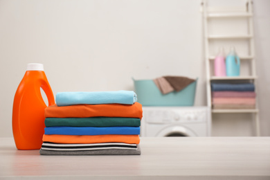 Stack of fresh laundry and detergent on white table in bathroom. Space for text