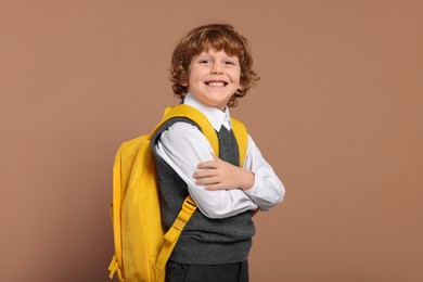 Photo of Happy schoolboy with backpack on brown background
