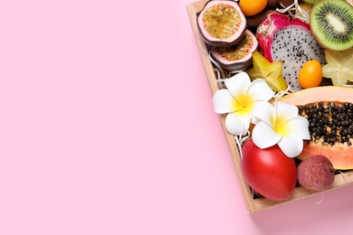 Different tropical fruits in wooden box on pink background, top view. Space for text