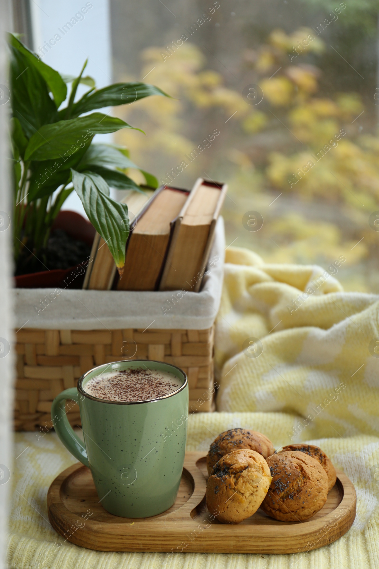 Photo of Cup of tasty hot drink and cookies near books on windowsill. Autumn coziness