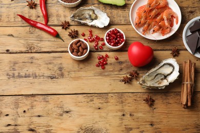 Photo of Natural aphrodisiac. Different food products and heart model on wooden table, flat lay. Space for text