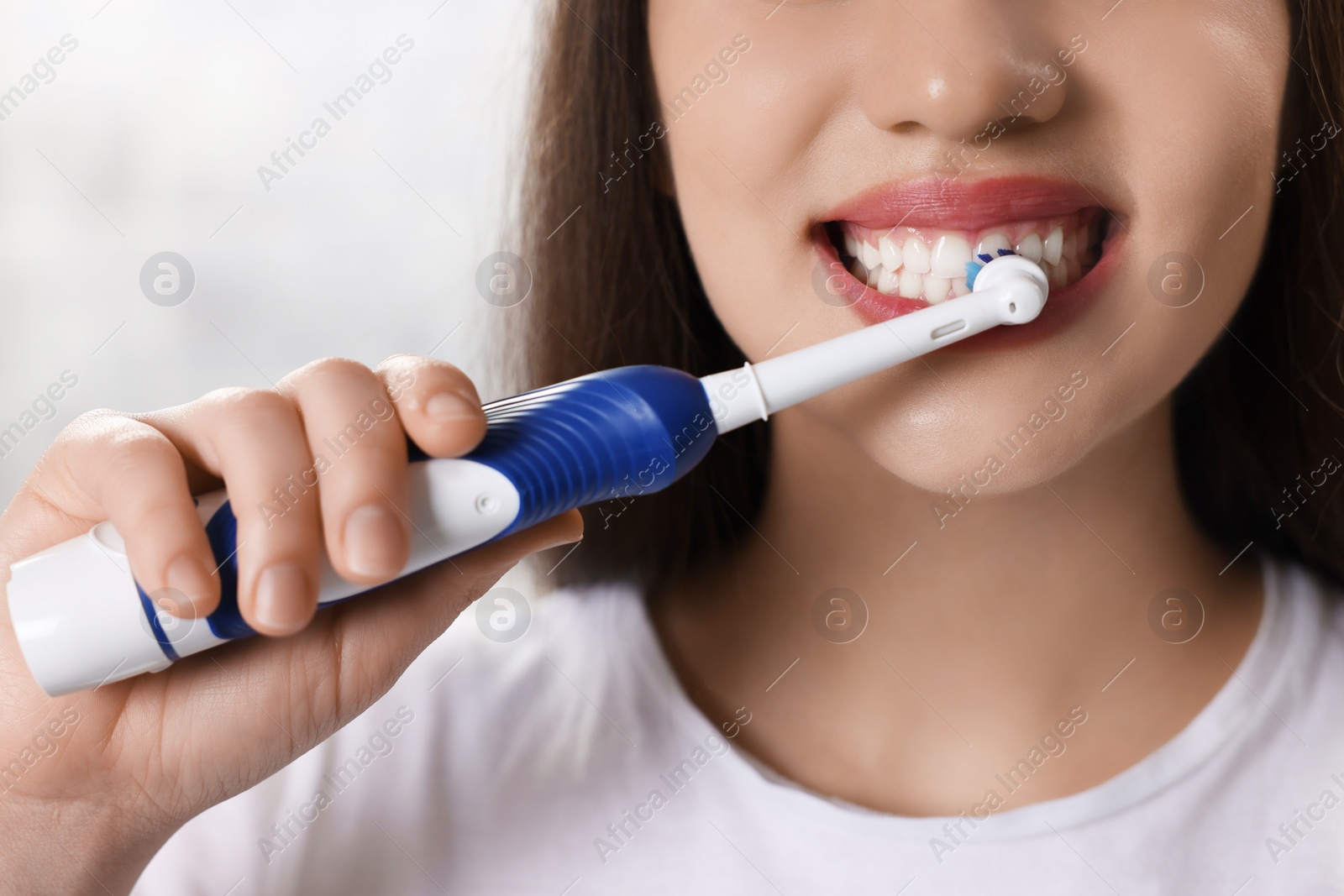 Photo of Woman brushing her teeth with electric toothbrush indoors, closeup