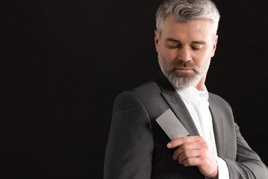 Handsome businessman holding blank business card on black background. Space for text