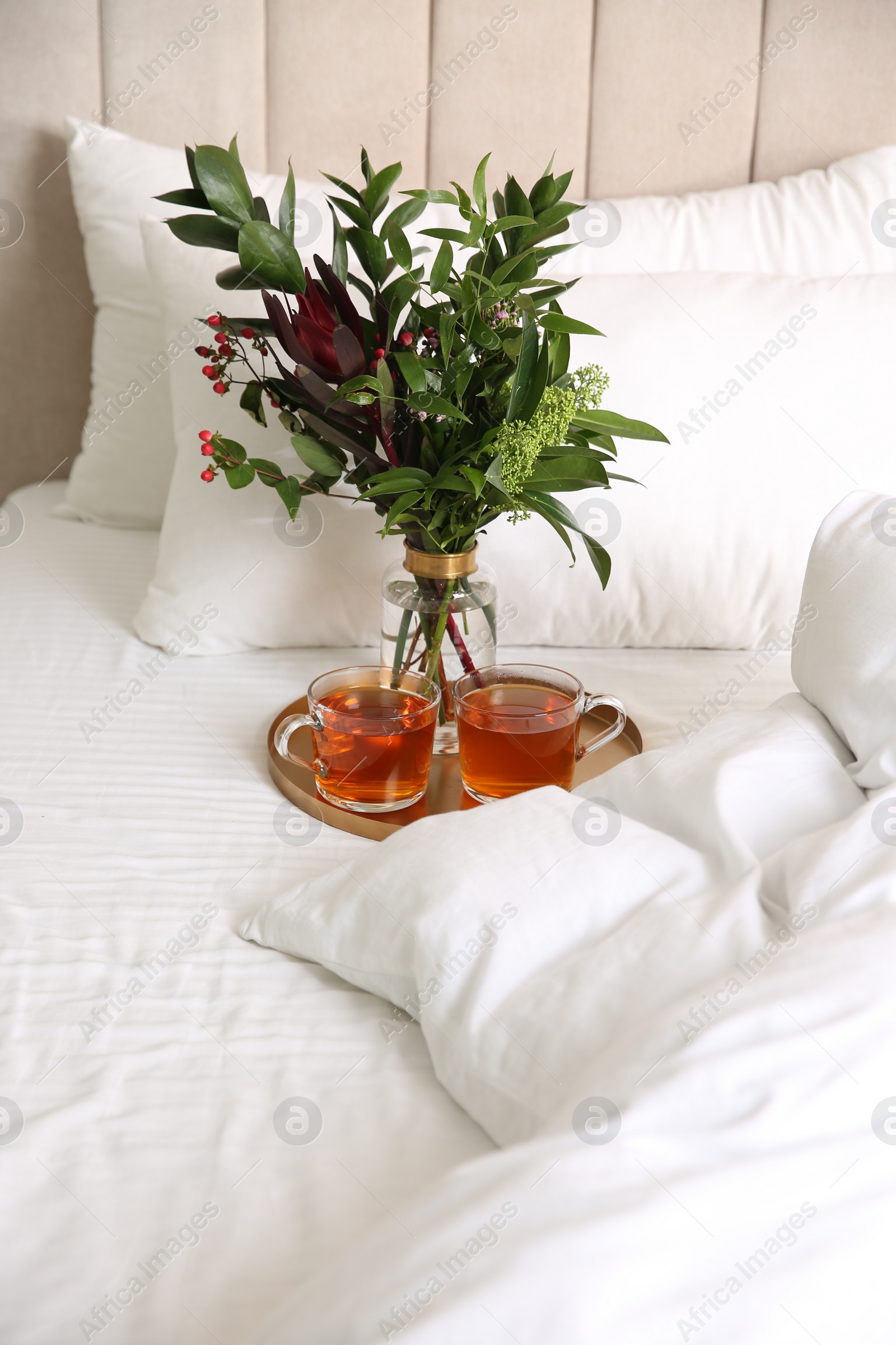 Photo of Tray with cups of tea and floral decor near soft blanket on bed