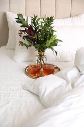 Photo of Tray with cups of tea and floral decor near soft blanket on bed