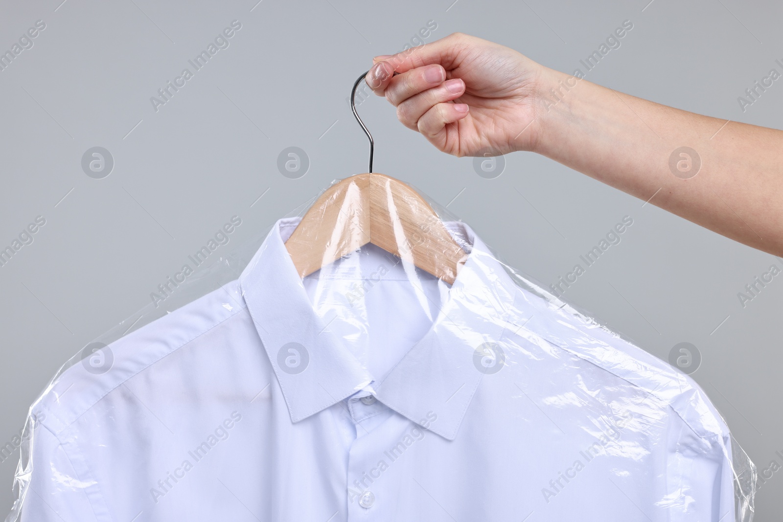 Photo of Dry-cleaning service. Woman holding shirt in plastic bag on gray background, closeup