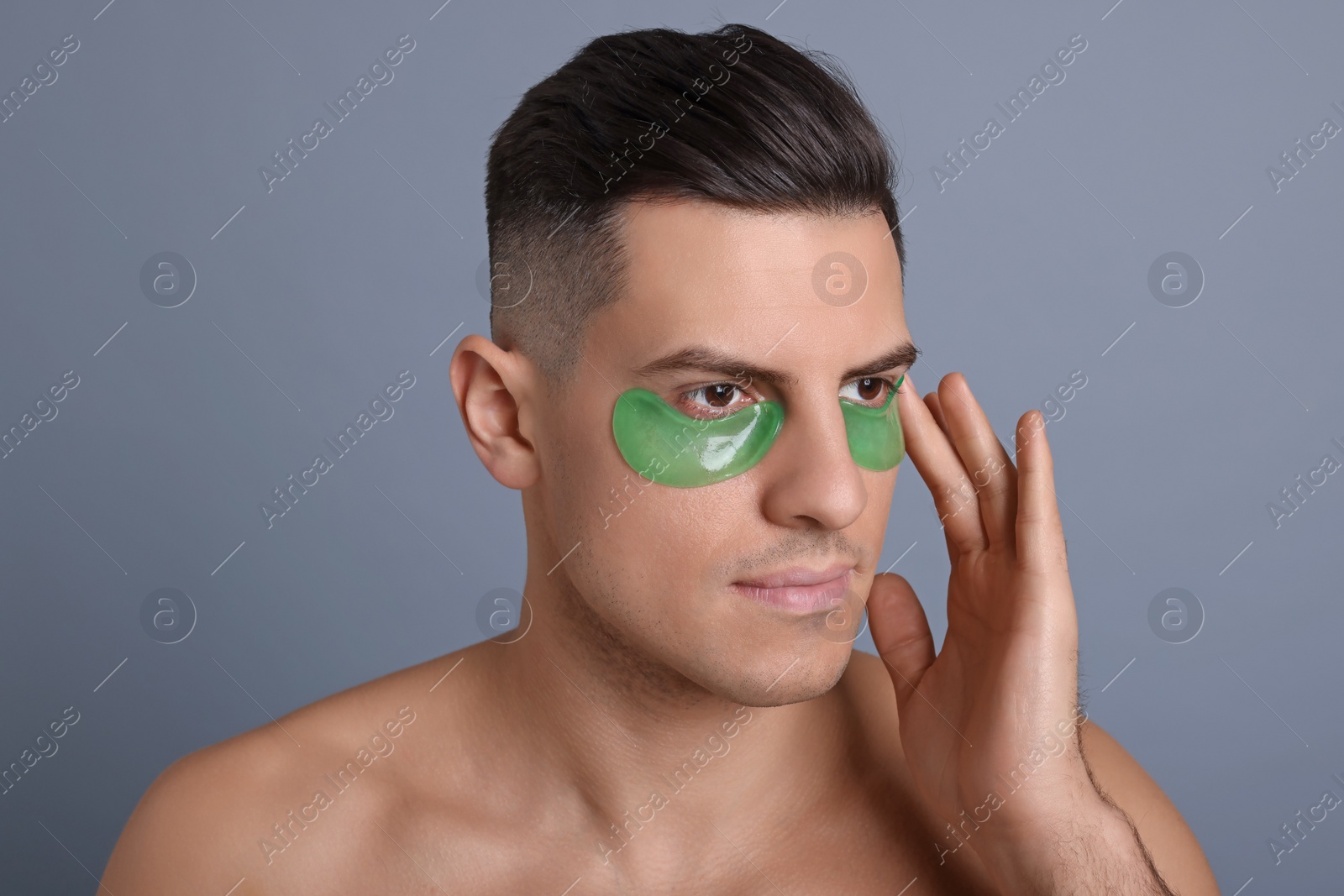 Photo of Man applying green under eye patch on grey background