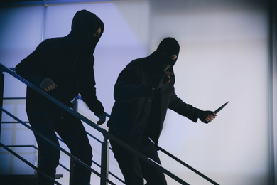 Photo of Men in masks with knife on stairs indoors. Dangerous criminals
