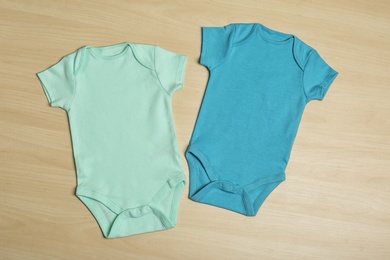 Cute baby onesies on wooden background, top view