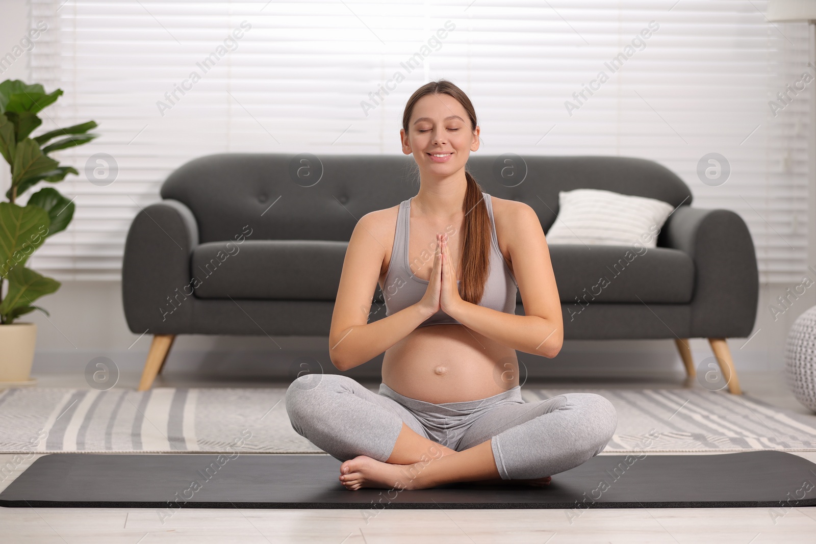 Photo of Pregnant woman meditating on yoga mat at home