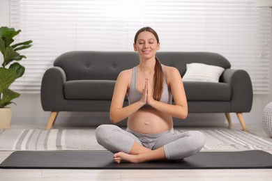 Pregnant woman meditating on yoga mat at home