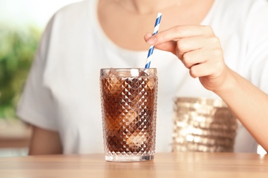 Photo of Woman with glass of tasty refreshing cola at table, closeup view