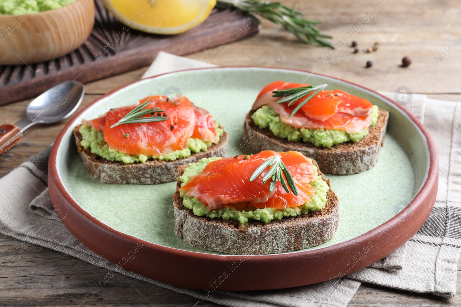 Photo of Delicious sandwiches with salmon, avocado and rosemary on wooden table