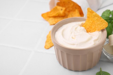 Photo of Delicious tofu sauce served with nachos chips on white tiled table, closeup. Space for text