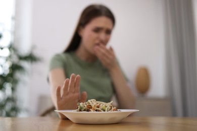 Photo of Young woman suffering from nausea at wooden table indoors, focus on food