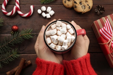 Photo of Woman with cup of delicious marshmallow cocoa at wooden table, top view