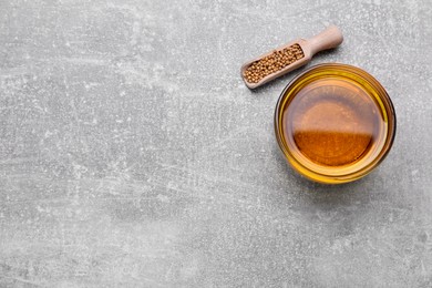 Photo of Bowl of natural oil and mustard seeds on light grey table, flat lay. Space for text