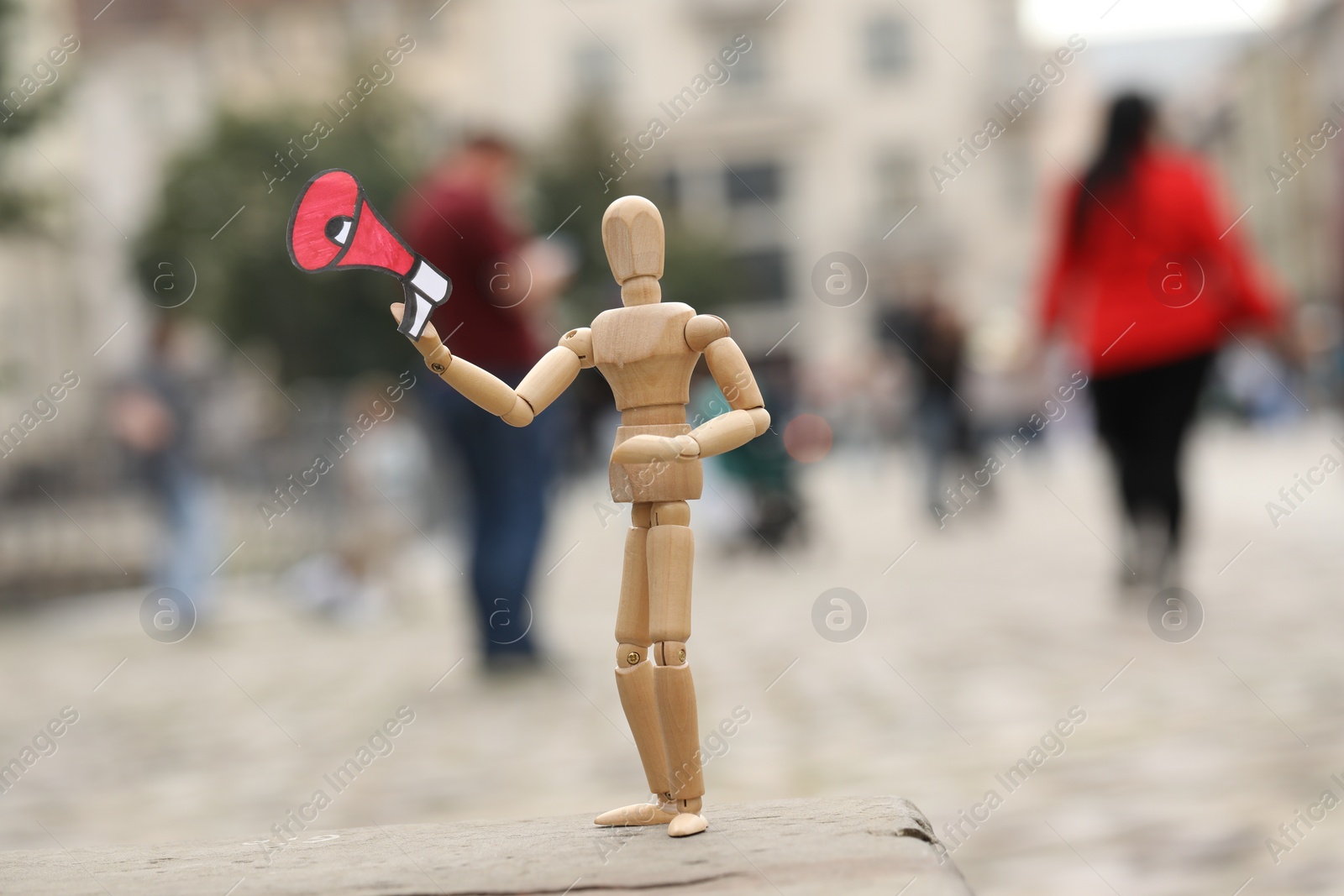 Photo of Wooden human figure with paper megaphone on city street, space for text