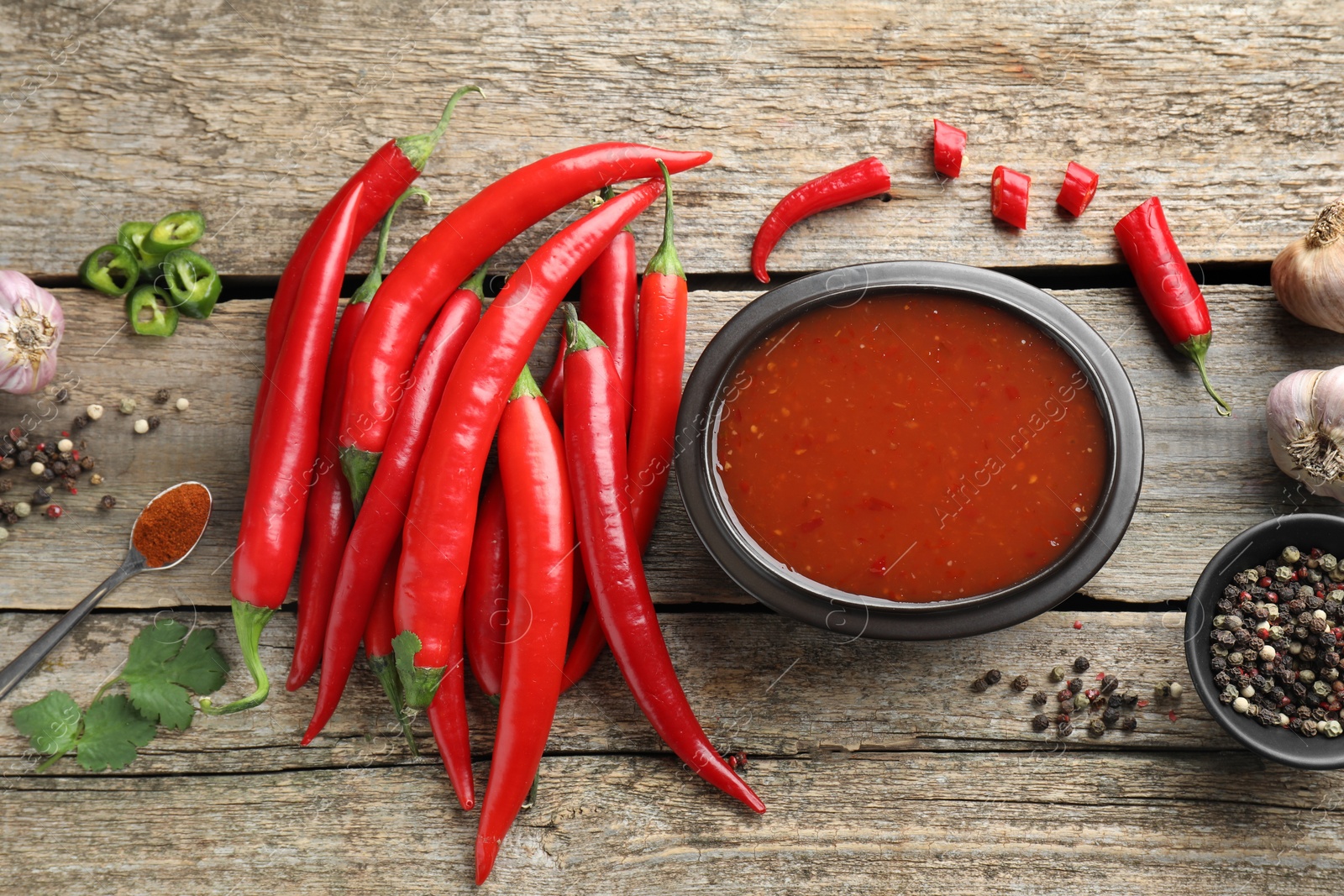 Photo of Spicy chili sauce in bowl and ingredients on wooden table, flat lay