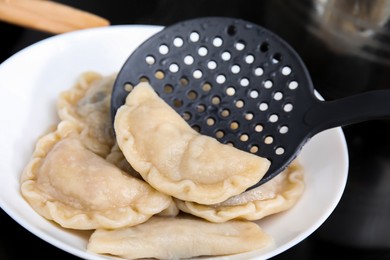 Photo of Putting delicious dumplings (varenyky) on plate, closeup