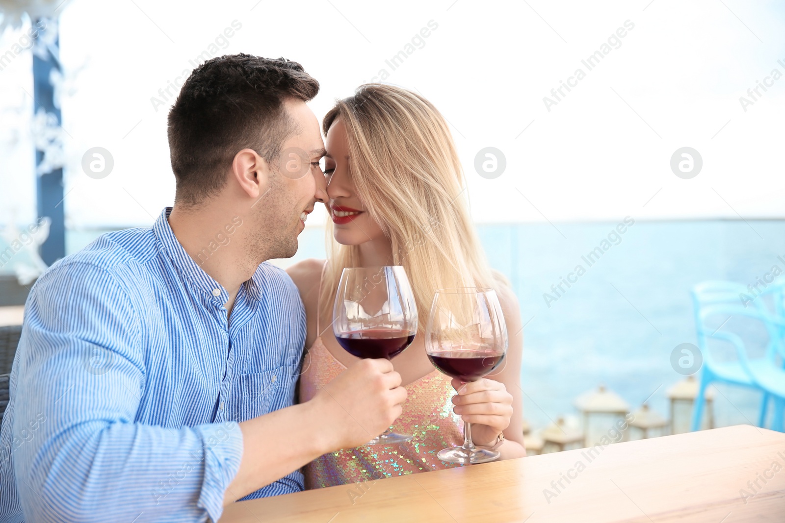 Photo of Young romantic couple with glasses of red wine at table