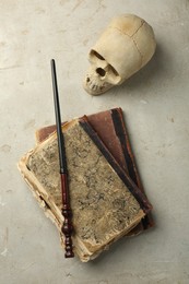 Photo of Magic wand, old books and human scull on light textured background, flat lay
