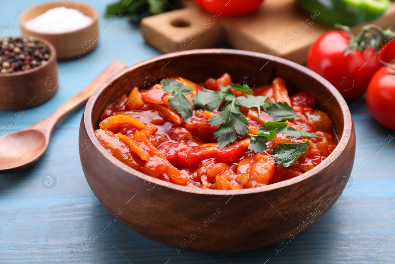 Photo of Bowl of delicious lecho with parsley on light blue wooden table, closeup