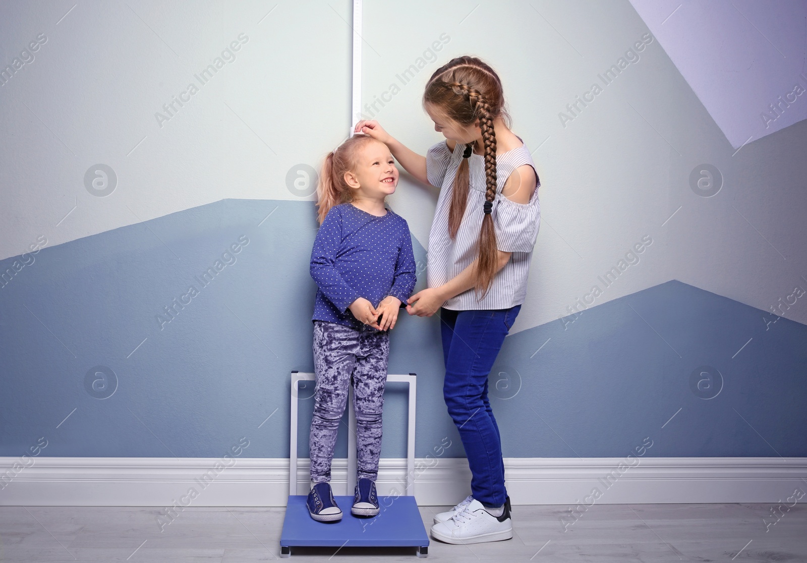 Photo of Little girls measuring their height near color wall