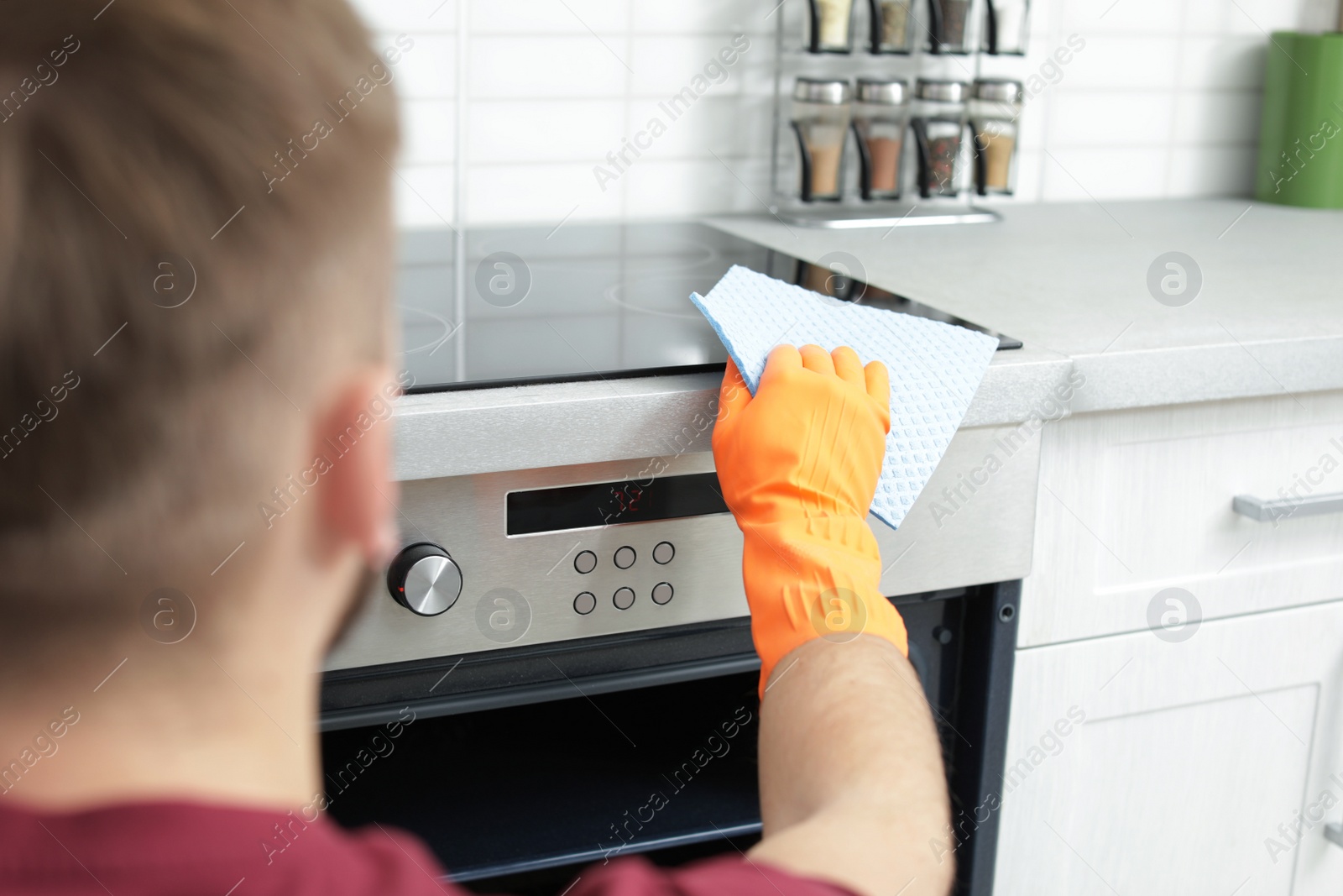 Photo of Young man cleaning oven with rag in kitchen