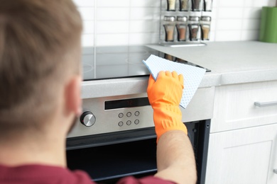 Photo of Young man cleaning oven with rag in kitchen